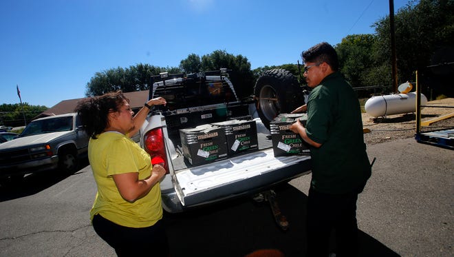 Customer Loretta Lujan talks on Thursday with Farmers Market produce worker Lamuel Pinto after receiving her order of roasted green chile at the grocery store in Flora Vista.