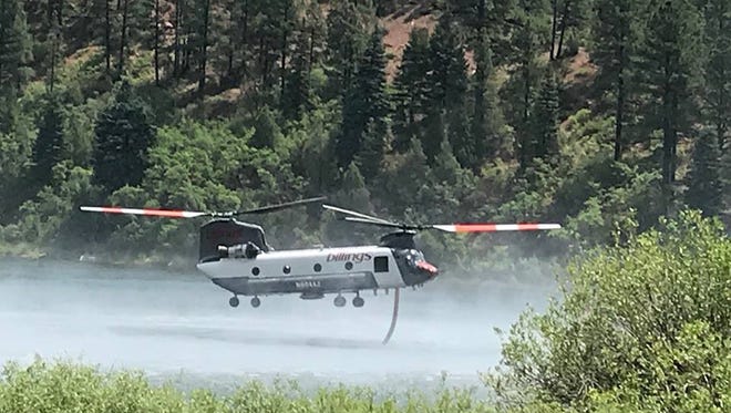 A Chinook helicopter that can drop up to 2,600 gallons of water hovers in the Fall Creek area, dipping its snorkel and pumping water up into an internal tank as it prepares to battle hotspots in the 416 Fire zone in this undated photo.