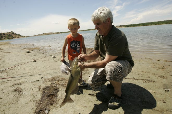 Benny Marionneaux unhooks a catfish he caught in August 2011 at Lake Farmington while his grandson, Jason Sanders, 4, watches.
