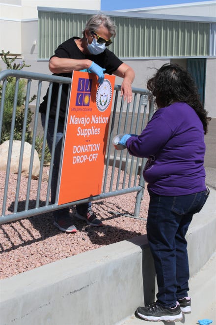 Volunteers Laura Darrow, left, and Shirley Hoskie, both employees of the San Juan College physical plant, post a sign May 8 on the college campus alerting drivers of the drop-off site for donations for Navajo Nation people affected by the COVID-19 shutdown.
