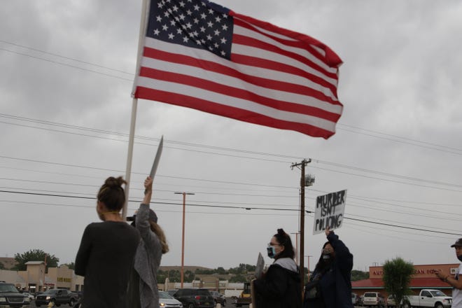 An American flag flies near a sign that draws attention to the mistreatment of African Americans by law enforcement during a peaceful protest in front of the Farmington Museum at Gateway Park on June 5 in Farmington.