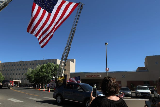 A car displaying the American flag and the Army flag drives by San Juan Regional Medical Center, Sunday, June 14, 2020, as onlookers gather to honor the late paramedic Glovis Foster and to thank him for his service to the community. He died June 12, 2020, in Albuquerque after battling COVID-19.