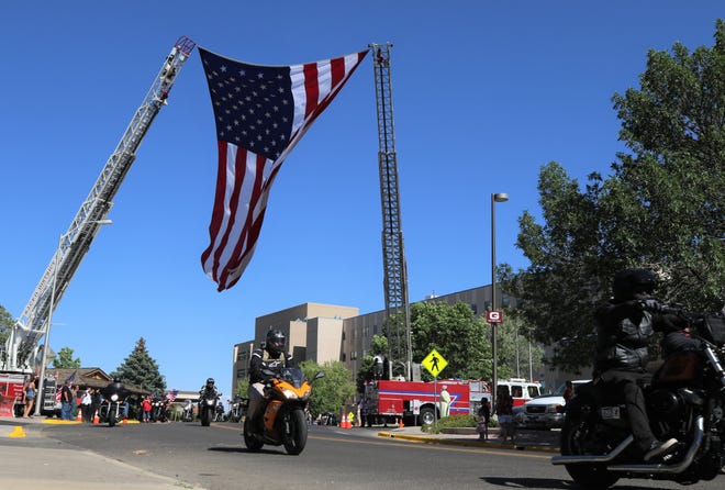 Motorcyclists participate in a procession to bring the body of paramedic Glovis Foster back to Farmington. The procession passed under a flag, Sunday, June 14, 2020, hung between two fire trucks in front of San Juan Regional Medical Center while a musician played the bagpipe.