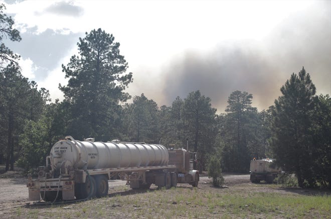 Smoke from the Wood Springs Two Fire rises in the background on June 29 as trucks sit parked along Navajo Route 7 in the Fluted Rock area near Sawmill, Arizona.