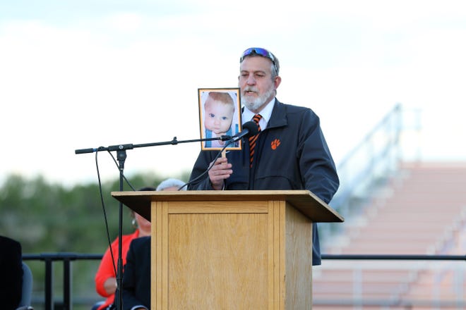 Aztec High School History Teacher and Wrestling Coach Monte Maxwell holds up a baby photo of his daughter Jocelyn Maxwell as he introduces her as Salutatorian on May 21 during the 2021 commencement ceremony at Fred Cook Memorial Stadium.