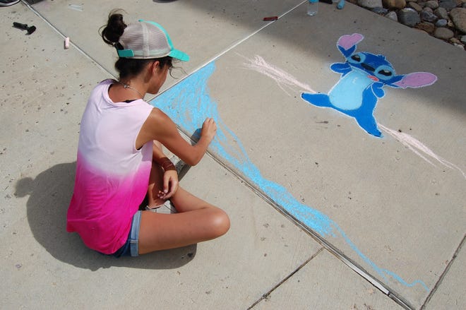 Lilly Yocum uses blue chalk to fill in a beach scene for her entry in the Chalk Art Festival outside the Farmington Public Library on June 10.