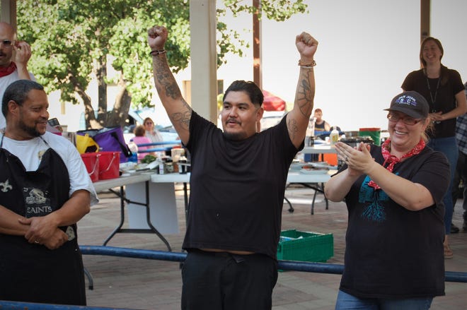 Chef Justin Pioche raises his arms in celebration while fellow competitors Neil Johnson, left, and Jacqueline Montoya watch after Pioche was named the winner of the cook-off at the Northwest New Mexico Local Food Summit on July 15 in Orchard Park in downtown Farmington.