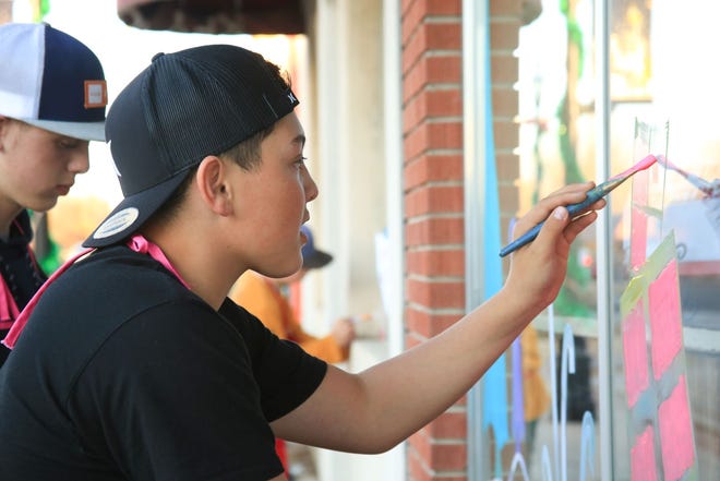 Luke Clugston, left, and Jayden Fitzgerald paint a Whoville-inspired scene on the window of an Aztec business as part of the "Find the Grinch" contest.