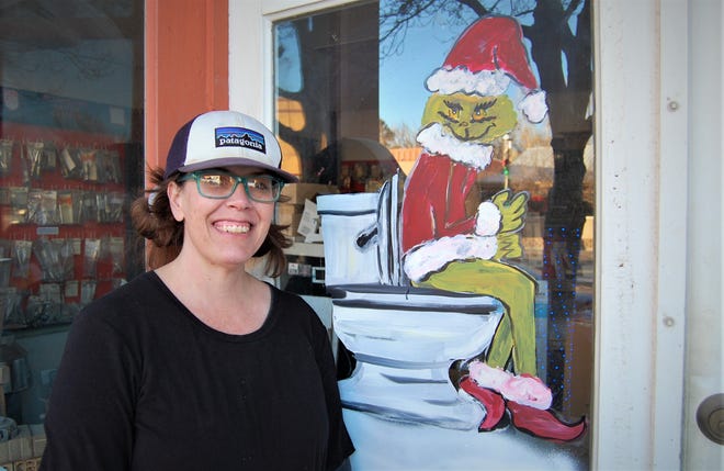 Christy Clugston of Inspire heART poses with one of her paintings of the Grinch in the window of Aztec Plumbing & Supplies that she did for the "Find the Grinch" contest.