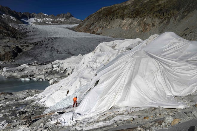 In this file photograph taken on Oct. 27, 2021, a man works at the Rhone Glacier which is partially covered with insulating foam to prevent it from melting due to global warming near Gletsch, Switzerland.
