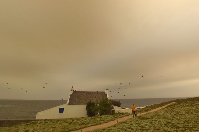 In this file photograph taken on Oct. 16, 2017, a woman walks on the beach in Quiberon, western France, as the sky turned a yellow-ochre color due to sand from the Sahara desert and dust from wildfires in Portugal being carried by winds from Storm Ophelia.