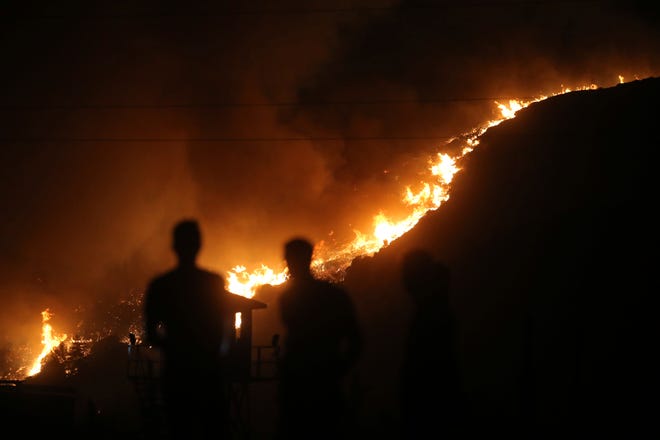 People stand in front of Kemerkoy Thermal Power Plant with a blaze from a wildfire approaching in the background, in Milas, Mugla, Turkey, Aug. 3, 2021. A panel of scientists convened by the UN has published a report on the impacts of climate change on the planet, including on the natural world and human civilization.